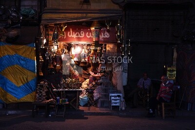 Two men sitting in front of a street shop drinking hookah, street, decoration lights