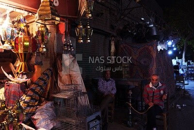 Two men sitting in front of a street shop drinking hookah, street, decoration lights