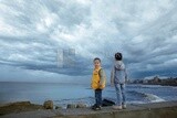 Two children on the beach fence in front of the sea