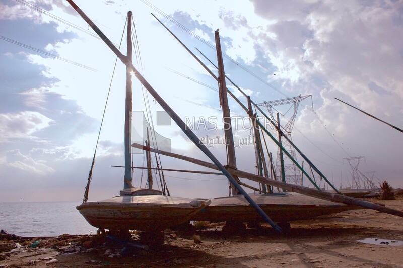 Group of old fishing boats stand off the shore next to the electricity towers during the day