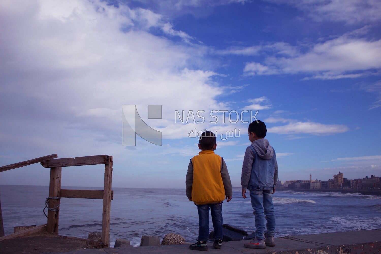Two children on the beach fence in front of the sea