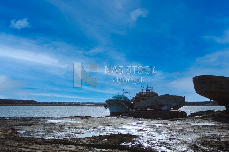 Man walks on the seashore in front of a group of large fishing boats parked on the shore