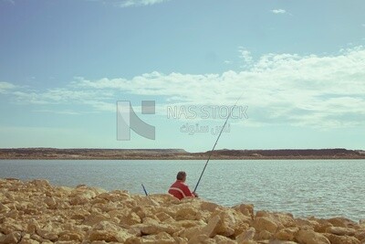 Man wearing a red jacket sits in front of the beach of the city of Burullus fishing