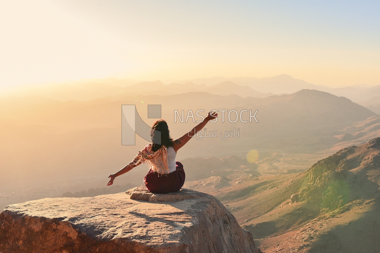 Woman with hands up sitting on top of mountain