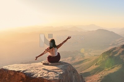 Woman with hands up sitting on top of mountain