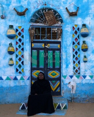 Nubian woman sitting in front of her colorful house in the Nubian style, Aswan, Egypt