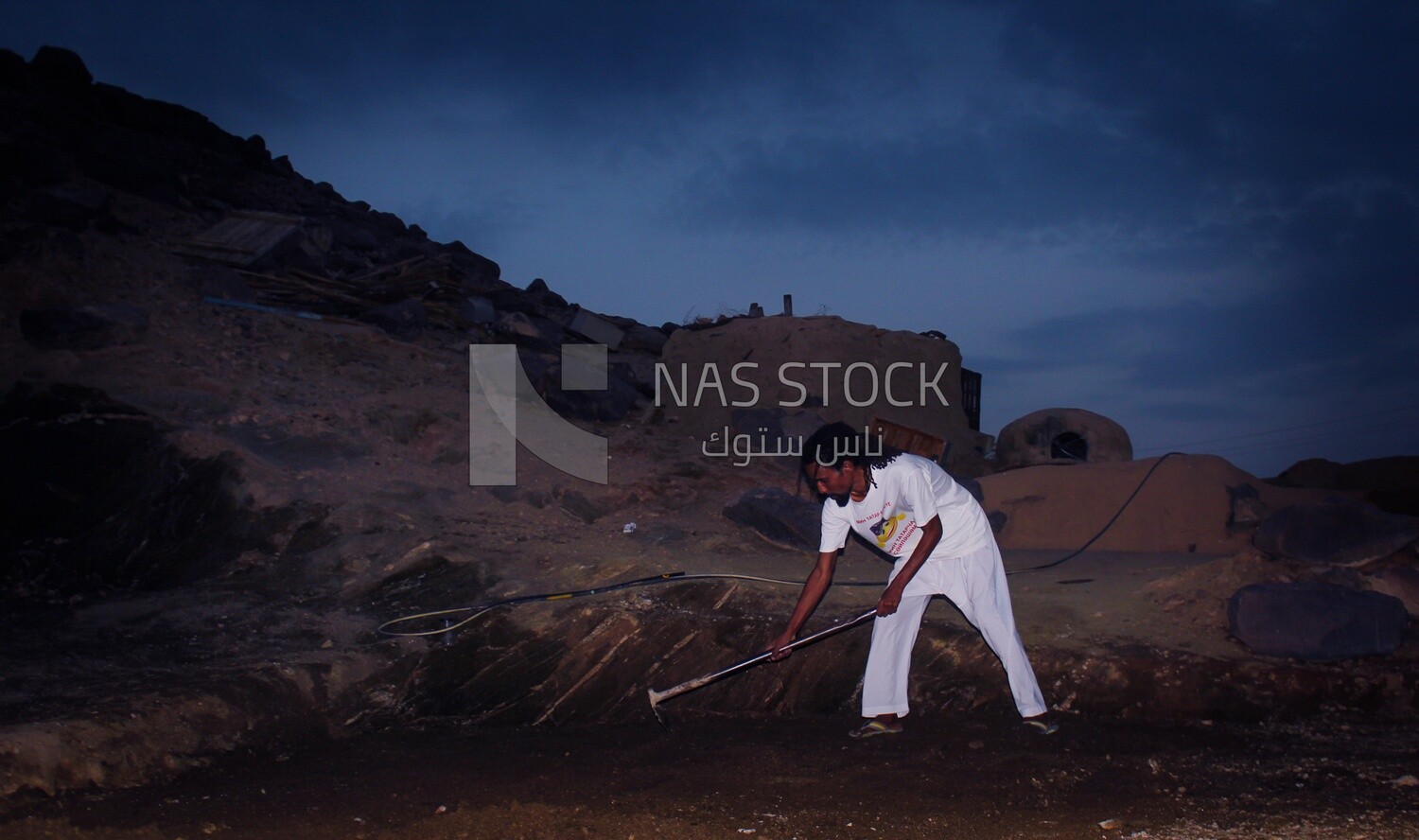 Young Nubian man digs the ground with an ax