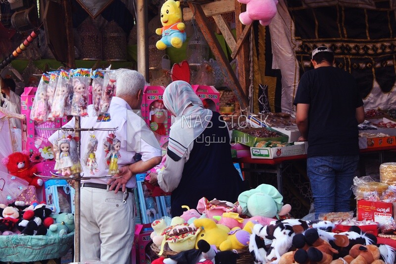 زوج مع زوجته واقفاً يشتري دمية المولد في الشارع، حلويات مصرية بمناسبة المولد النبوي الشريف