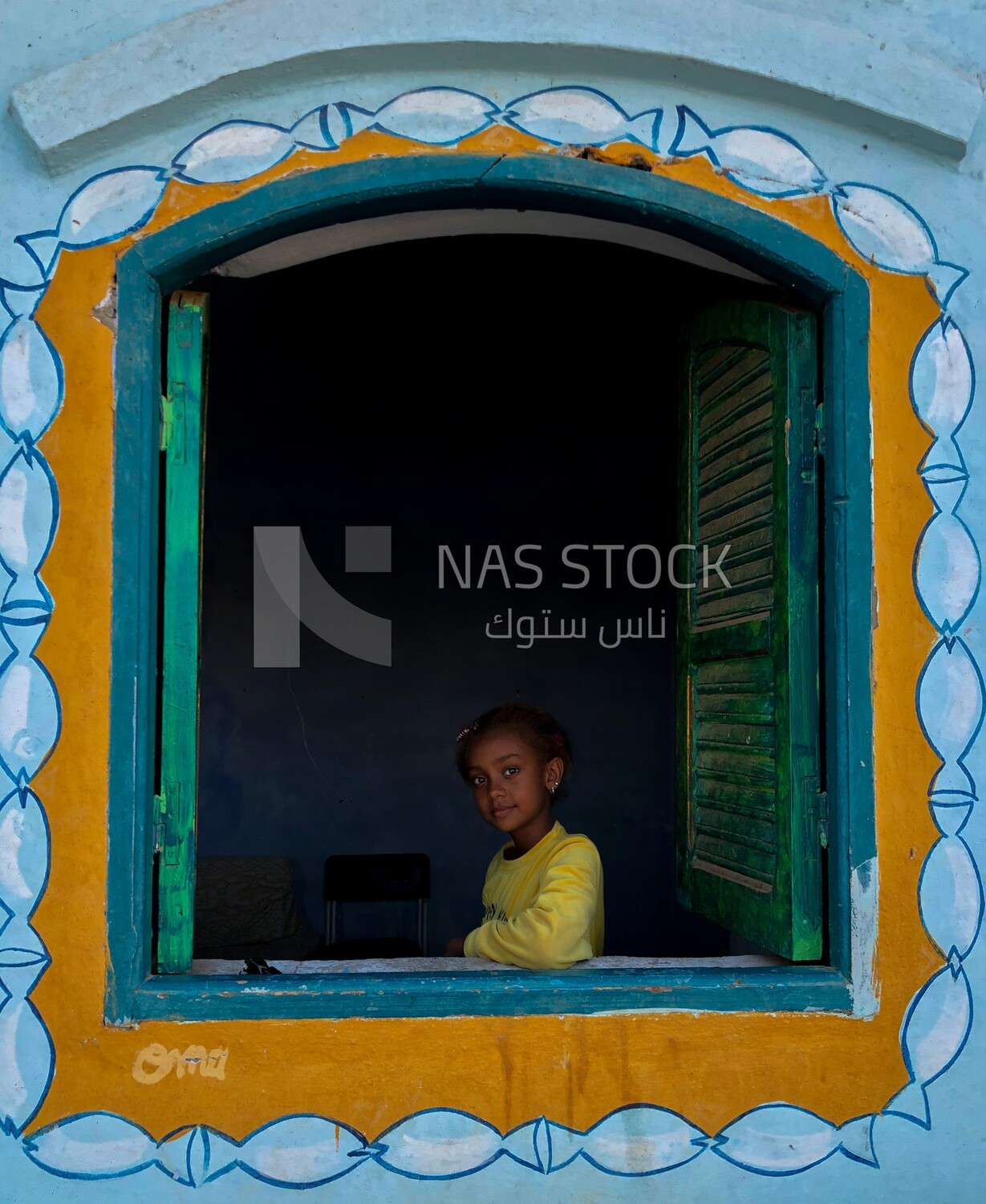 Beautiful girl with childish features stands in the window, Nubia, Egypt