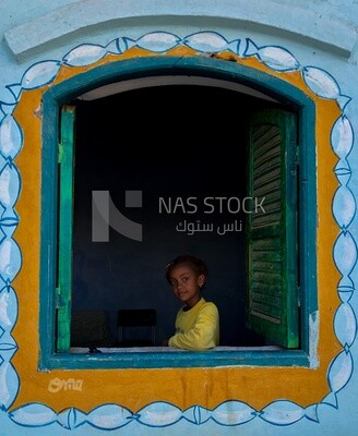Beautiful girl with childish features stands in the window, Nubia, Egypt