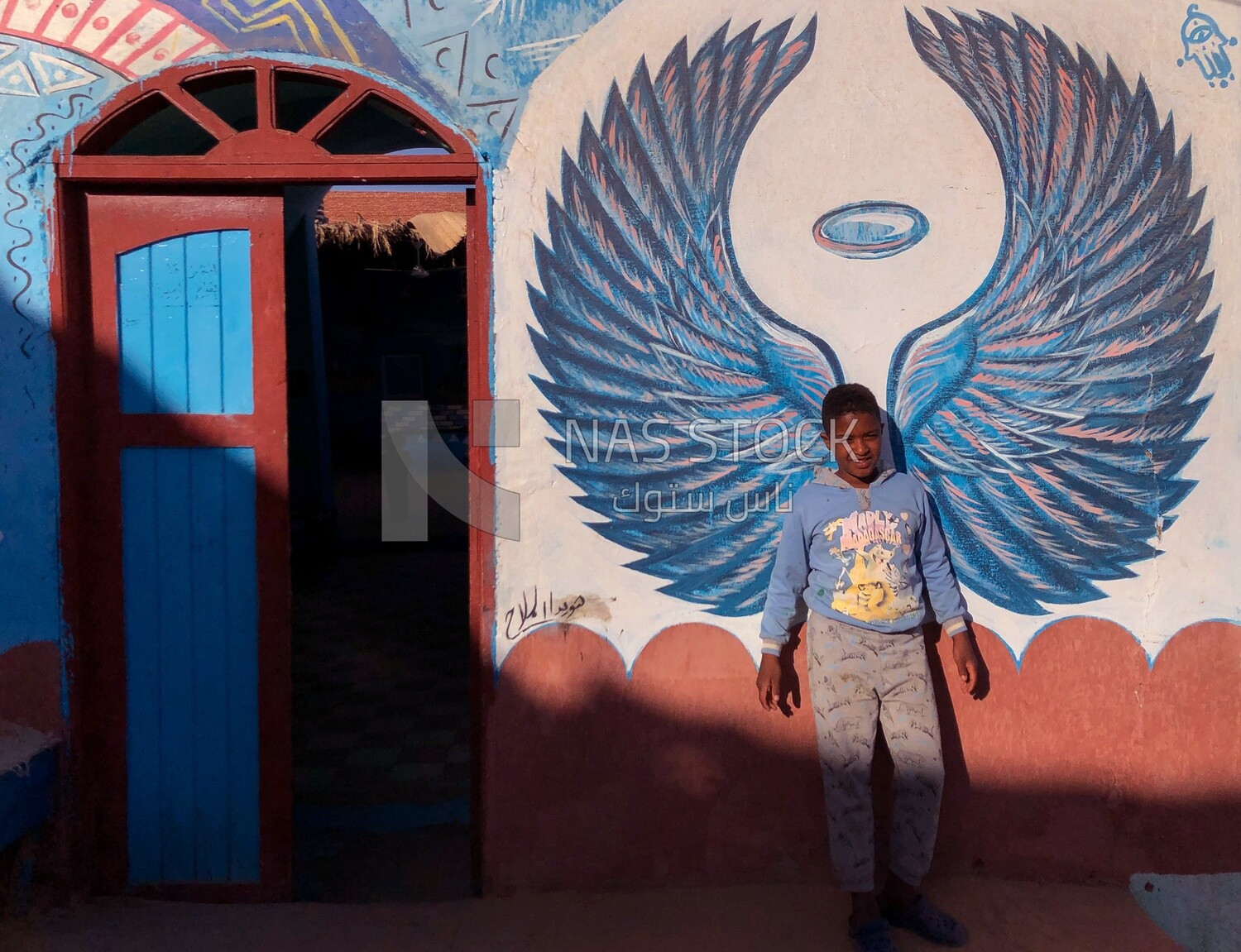 Nubian child takes a picture with a drawing of wings on the wall, Aswan, Egypt