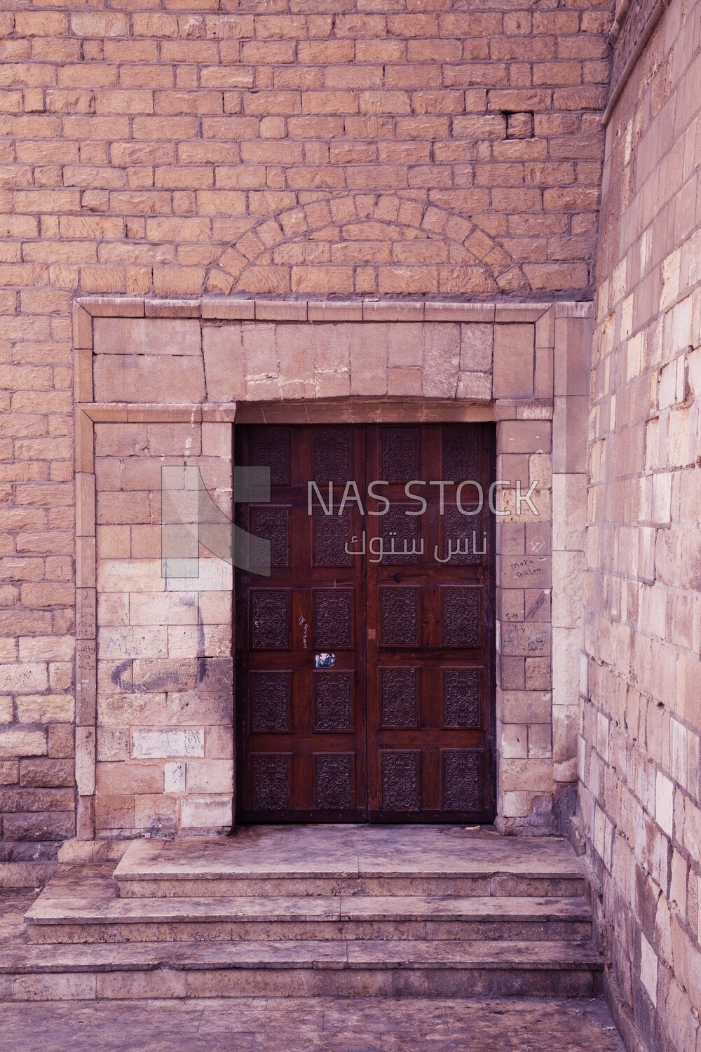 Wooden ornate engraved red door on bricks stone wall
