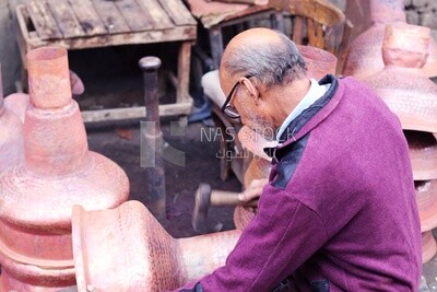 Man carrying a hammer works on aluminum vessels, Ahmed Al-Badawi