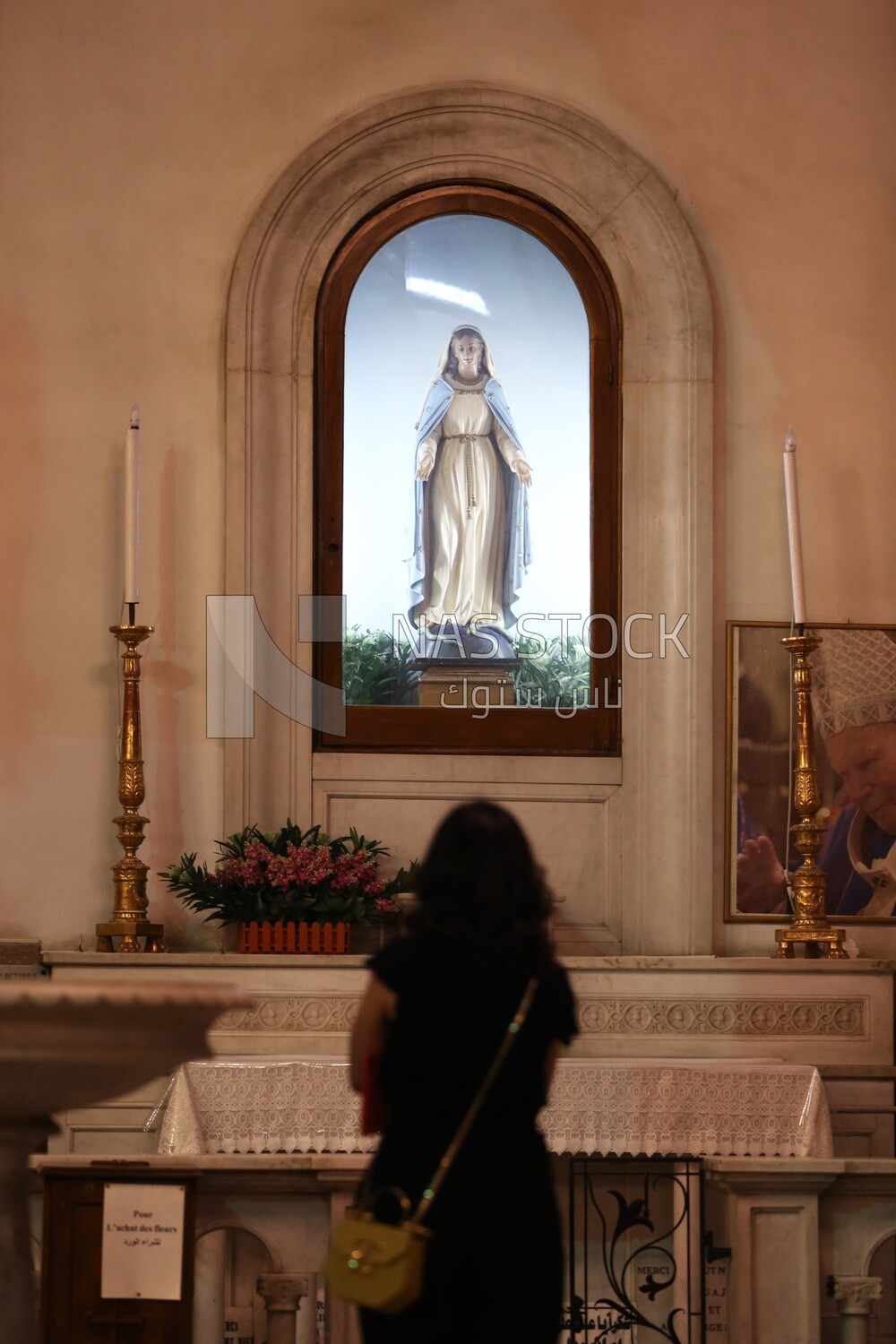 Woman stands worshiping in front of the statue of the Virgin Mary in the church