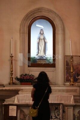Woman stands worshiping in front of the statue of the Virgin Mary in the church