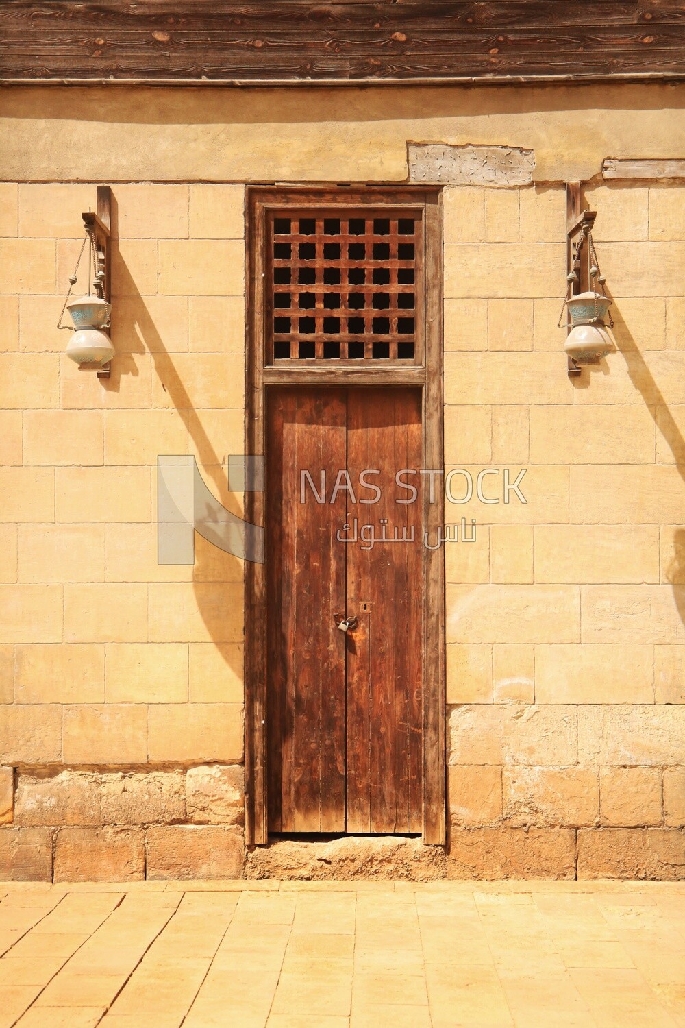 Wooden closed door and two Arabic glass street lanterns hung on a wooden pole, The School and dome of Sultan Al-Nasir Qalawun
