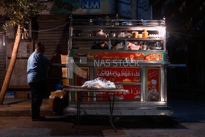 Man standing in a food cart selling food to people on the street