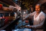 Man standing in a food cart selling food to people on the street