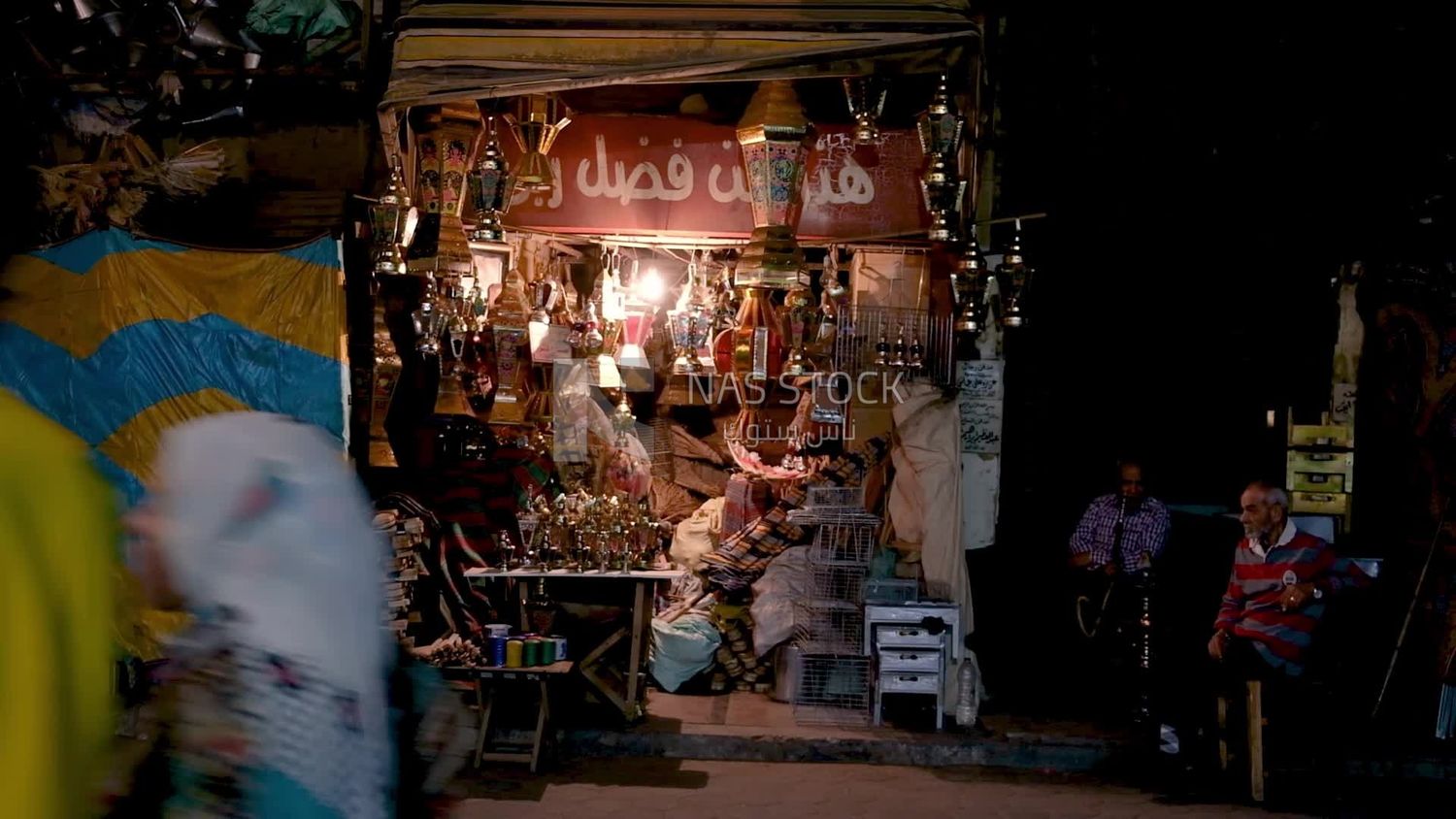 Two men sitting in front of a street shop drinking hookah, street, decoration lights