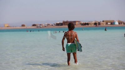 Young man in a swimsuit holds a surfboard ready to go water skiing