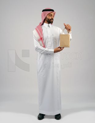 رجل خليجي يمسك بيده كيس من اكياس التسوق