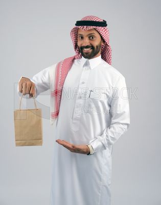 رجل خليجي يمسك بيده كيس من اكياس التسوق