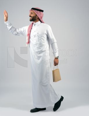رجل خليجي يمسك بيده كيس من اكياس التسوق