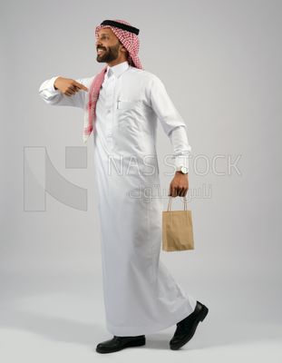 رجل خليجي يمسك بيده كيس من اكياس التسوق