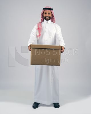 شاب خليجي بالزى السعودى و الشماغ يحمل صندوق مشتريات الاونلاين ، شركات الشحن، خدمات التوصيل المنزلي، التسوق الذكي، استلام الطلبات , شركات الشحن و التوصيل