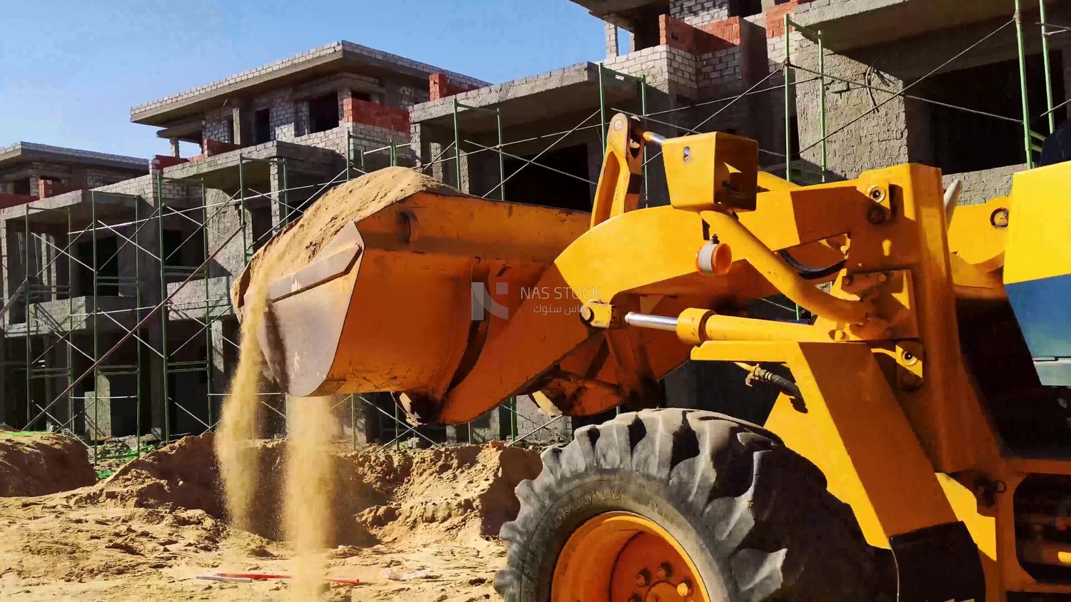 Bulldozer carries sand into a construction site where it transports it to be mixed with cement