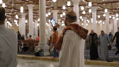 Man in the mosque, holding his mobile, praying on the prayer rug, performing the obligatory prayer in the mosque, worship and draw close to God