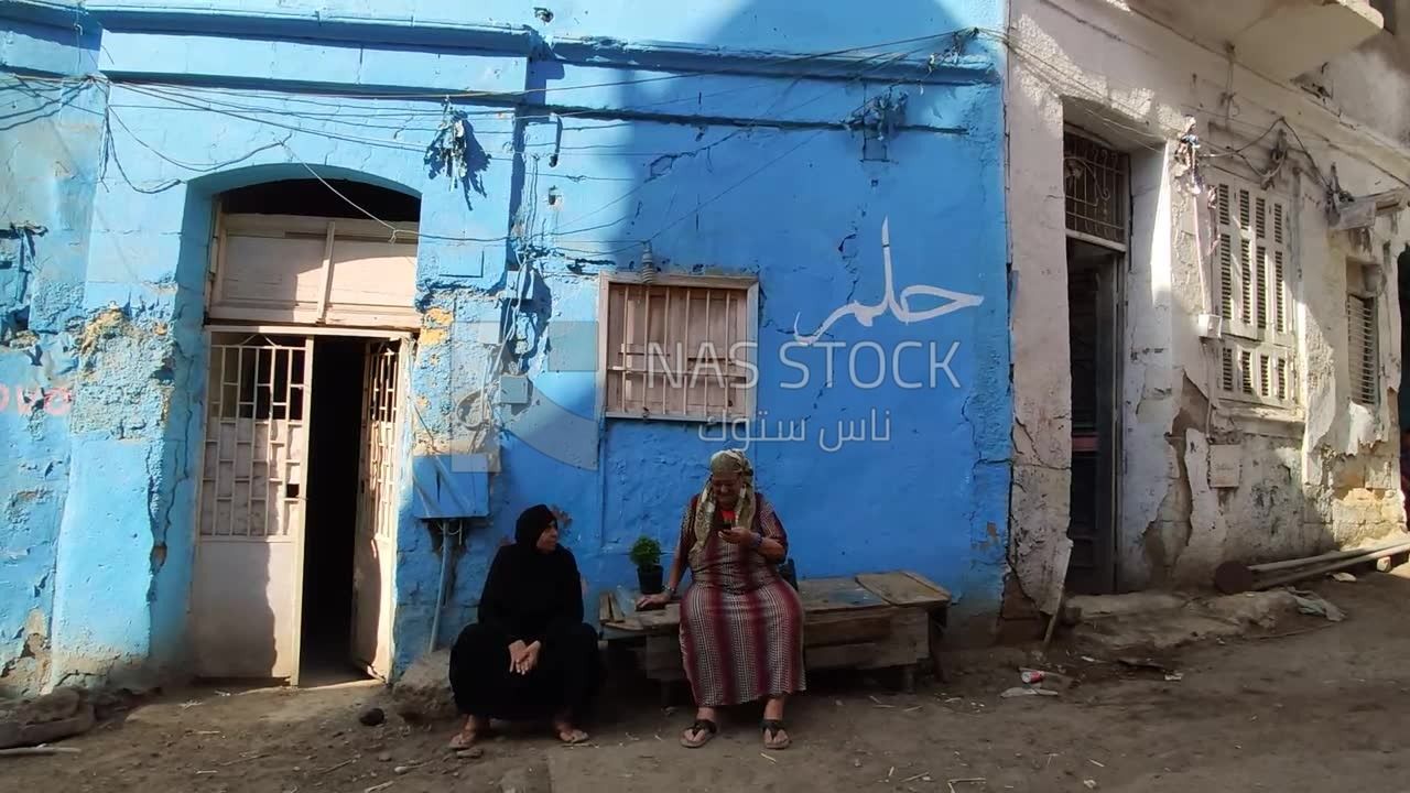 Two elderly women are sitting in front of a house on the street