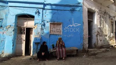 Two elderly women are sitting in front of a house on the street