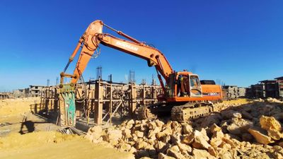 Worker drives an excavator and breaks through the layers of the earth to dig a construction site