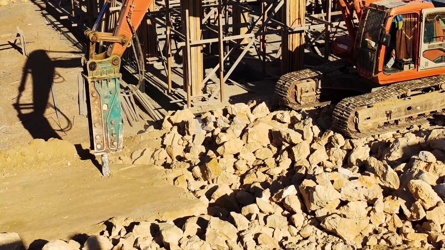 worker drives an excavator and breaks through the layers of the earth to dig a construction site