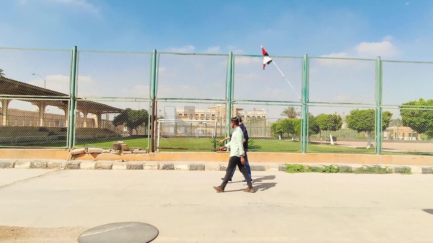 Two men are walking near a football field