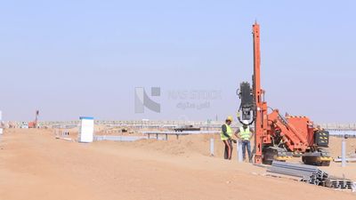 Two men wearing helmets and protective vests trying to operate a machine at the solar energy site