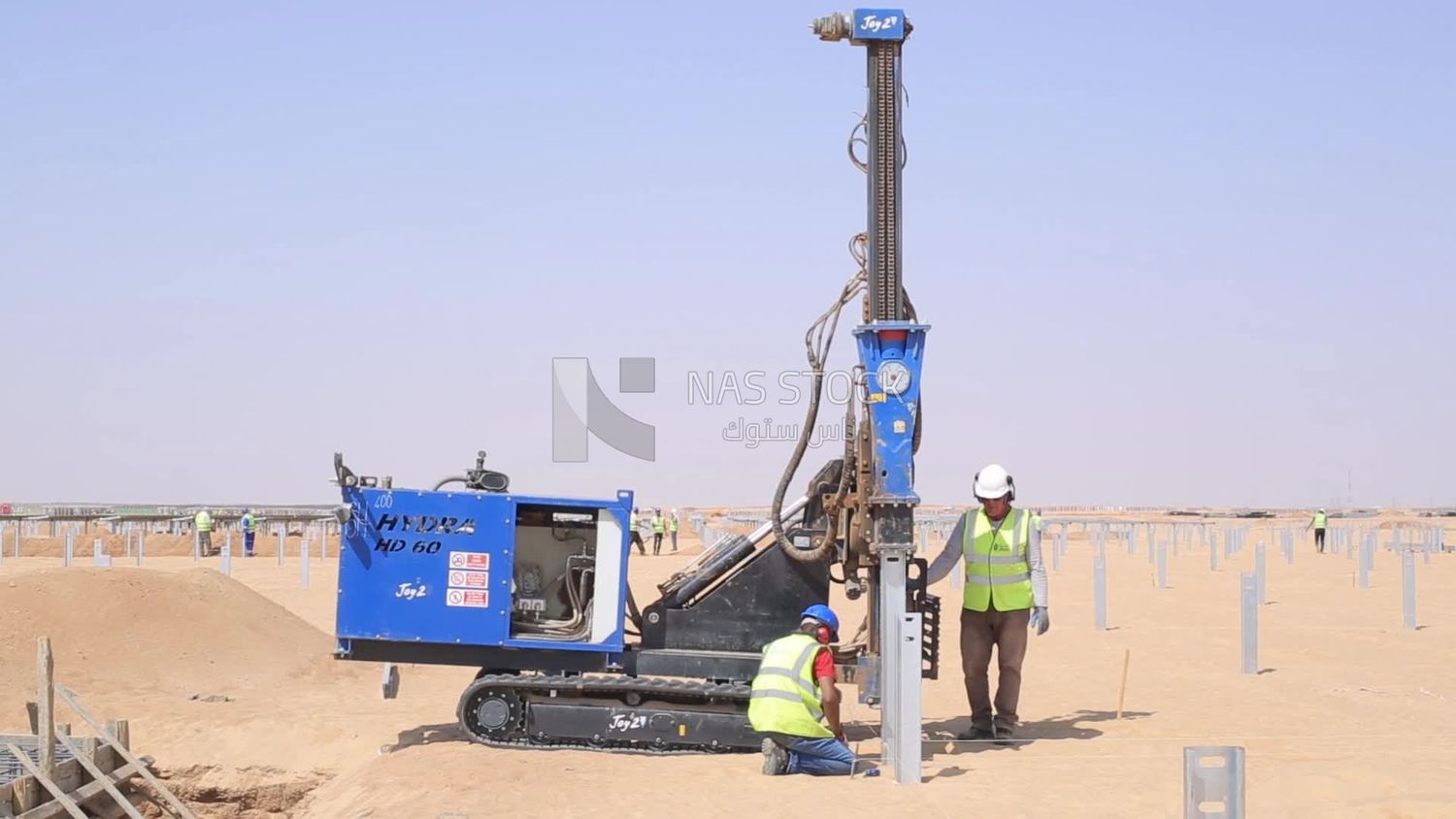 Two men wearing helmets and protective vests trying to operate a machine at the solar energy site