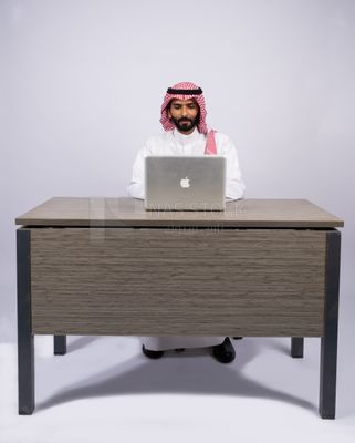 رجل خليجي يجلس على المكتب ويستخدم الكمبيوتر المحمول