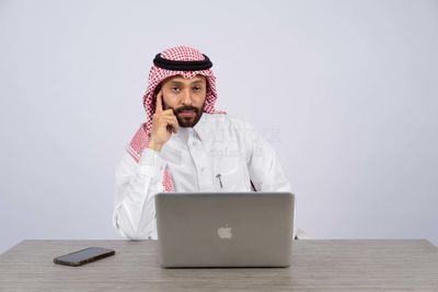 رجل خليجي يجلس على المكتب ويستخدم الكمبيوتر المحمول