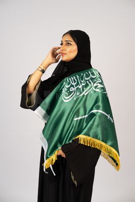 Saudi girl wearing the Gulf abaya and placing the Saudi flag on her shoulder