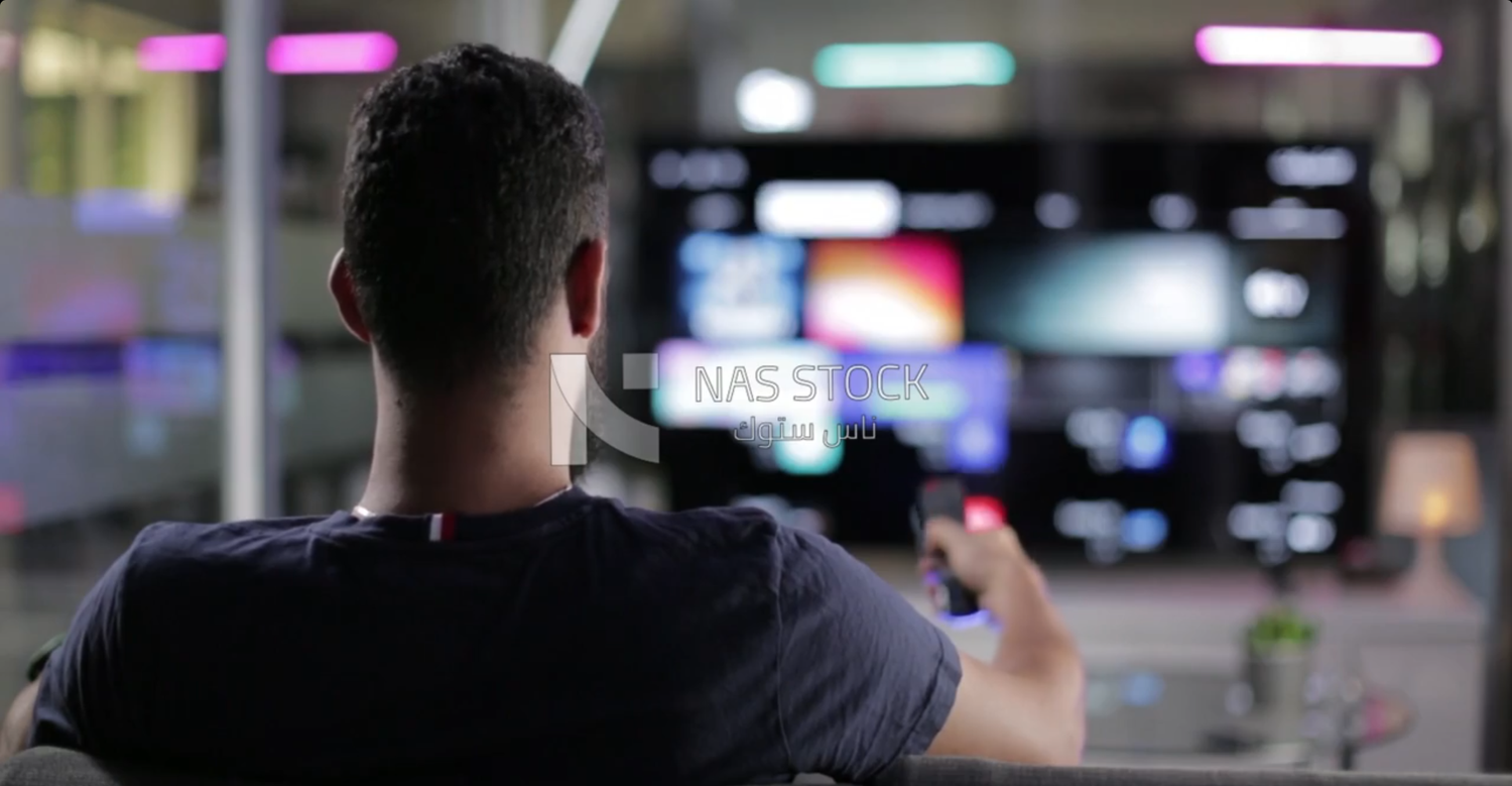 Young man sitting with his back watching TV and using the remote control
