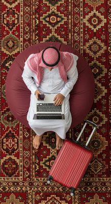 A Gulf man using a laptop with a red suitcase next to him