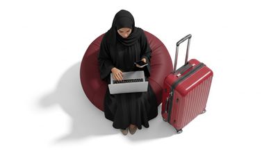 A Gulf girl using a laptop with a red suitcase next to her