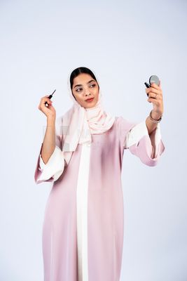 Gulf woman wearing an abaya and hijab, applying kohl