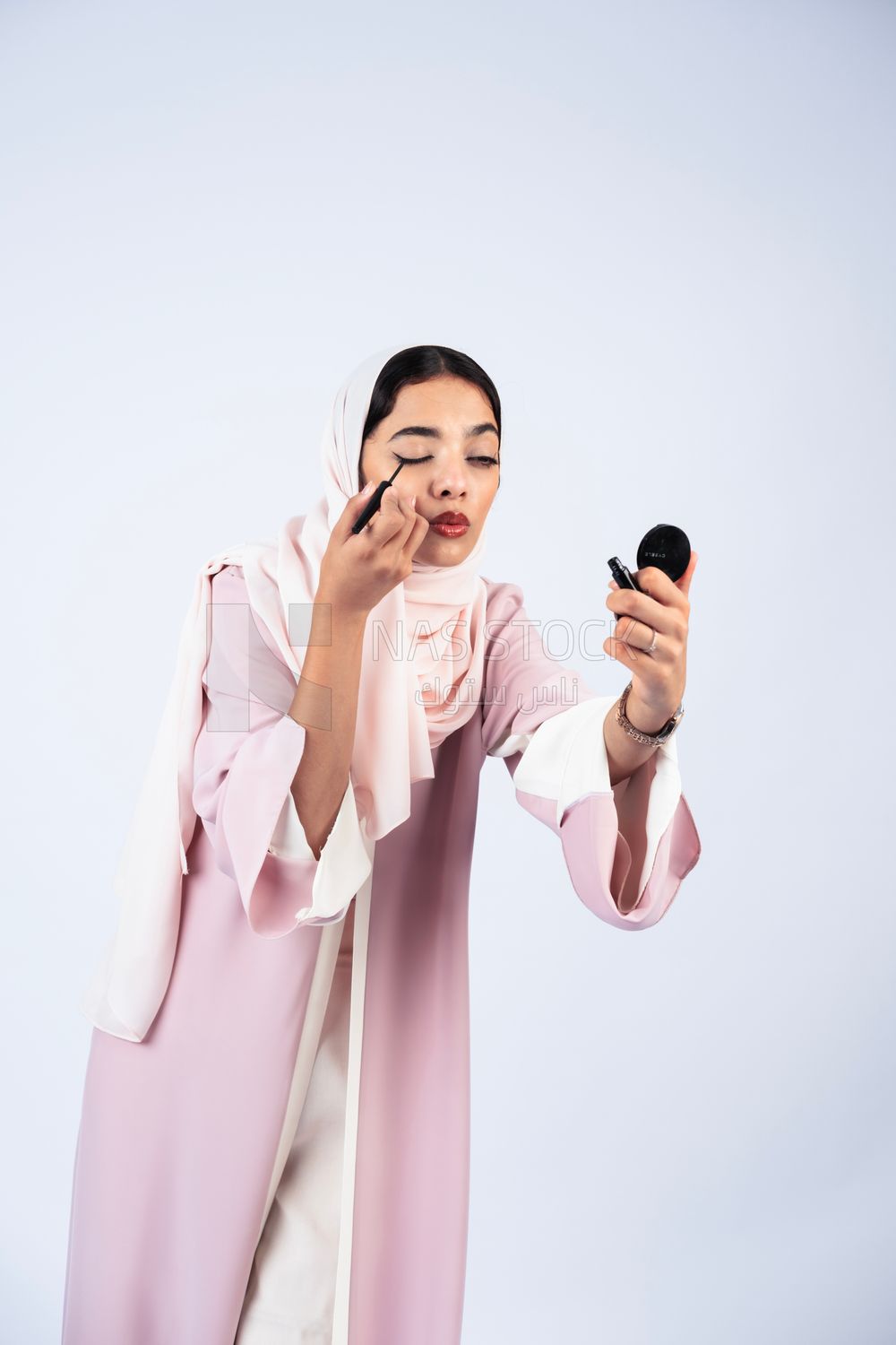 Gulf woman wearing an abaya and hijab, applying kohl