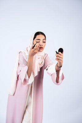 Gulf woman wearing an abaya and hijab, applying kohl