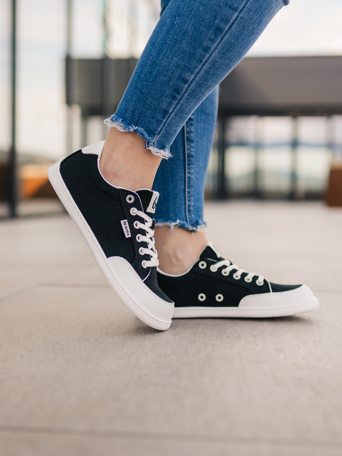 ragebild beLenka Rebound black-white – schwarzer Barfußsneaker mit weißer Zehenkappe und Sohle, kombiniert mit Jeans auf heller Terrasse