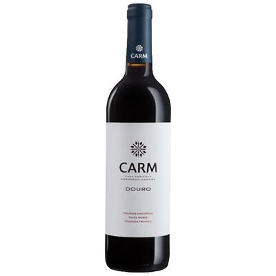  Uma garrafa do vinho tinto Carm 2021 ao lado de uma taça do vinho. Ao fundo, vislumbra-se a paisagem do Vale do Douro em tons quentes.
