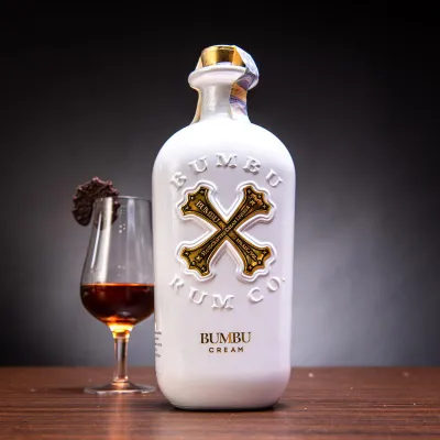 Uma elegante garrafa de Bumbu Cream 70cl, destacando a cor cremosa e o rótulo com o icônico "X" da Bumbu.